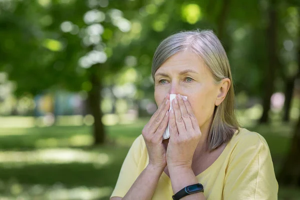 アレルギーのある公園の高齢者の女性は木の近くで鼻水とくしゃみをしています — ストック写真