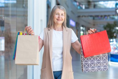 Güzel, son sınıf bir kadının portresi. Kağıt alışveriş torbalarını tutuyor ve gösteriyor. Ticaret merkezinden alışveriş yapar, alışveriş yapar. Alışverişten memnun, mutlu.