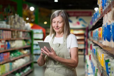 Kıdemli kadın danışman portresi, bakkal, süpermarket çalışanı. Tabletle duruyor, malları kabul ediyor, çekleri alıyor. İş kıyafetleriyle..