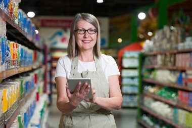 Gözlük danışmanı kıdemli kadın portresi, bakkal, süpermarket çalışanı. Tabletle duruyor, malları kabul ediyor, çekleri alıyor. İş kıyafetleriyle.