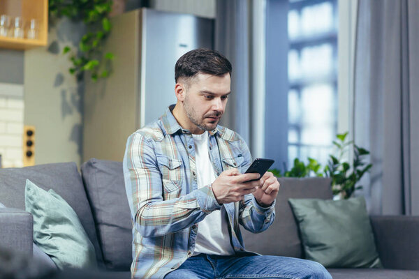 Портрет молодого красивого мужчины. Сидит дома на диване, разговаривает по телефону, пишет историю, машет руками, объясняет