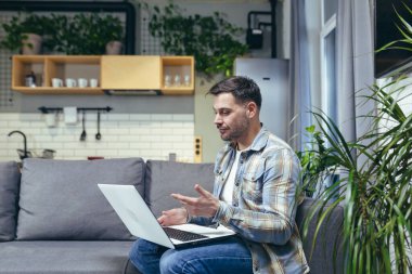 Adam evde çalışıyor, kanepede oturuyor, görüntülü konuşuyor, dizüstü bilgisayara bakıyor.