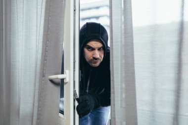 Siyah elbiseli erkek hırsız evin kilidini kırmaya çalışıyor.