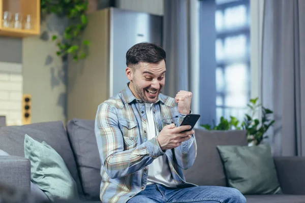 Happy Man Looks Phone Home Rejoices Success Victory — Stock Photo, Image