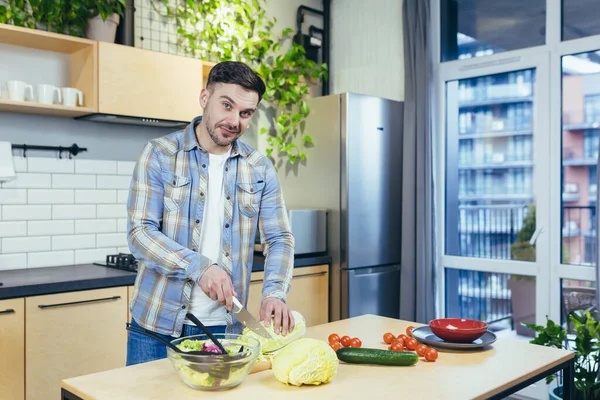 The man prepares healthy and healthy food at home, cuts vegetables for salad in the kitchen