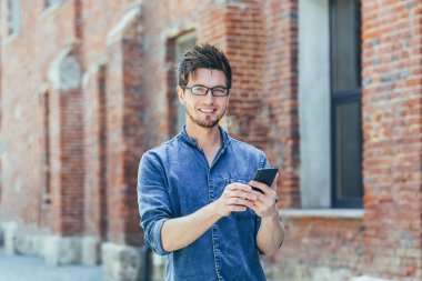 Öğrenci kampüsü dışında genç bir adam, öğrenci telefonda gülümsemeyi seviyor.