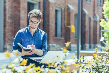 Kampüsteki genç öğrenci laptopta çalışıyor ve çalışıyor, ofis dışında günlük kıyafetler giymiş bir adam.