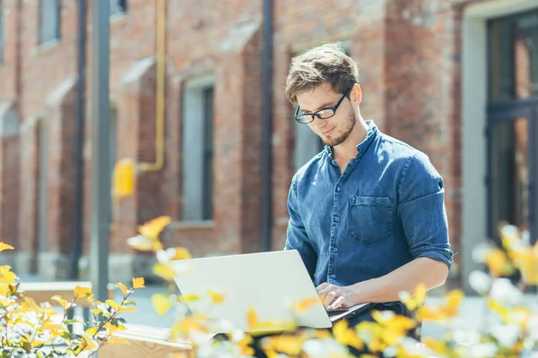 Ofisin yanında gözlüklü genç bir işadamı dizüstü bilgisayarla çalışıyor.