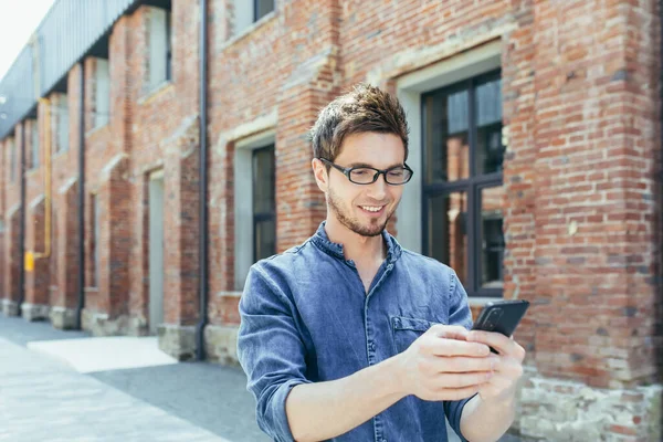 Kampüsün dışında elinde cep telefonuyla gülümseyen ve yürüyen genç bir öğrencinin portresi.