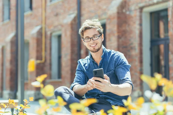 Ofisin dışında oturan genç işadamı telefonun keyfini çıkarıyor ve gülümsüyor