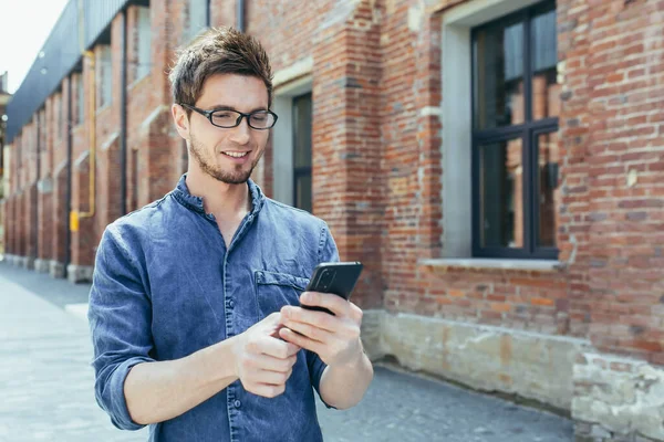 Young man outside student campus, student enjoys phone smiling