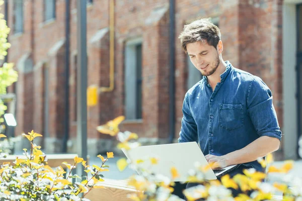 Kampüsteki genç öğrenci laptopta çalışıyor ve çalışıyor, ofis dışında günlük kıyafetler giymiş bir adam.