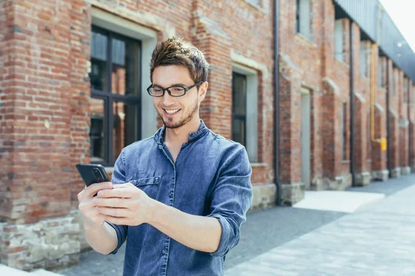 Young handsome young man with glasses travels to another country. Walks around the city and calls on a video call from a mobile phone to friends and family. He waves his hand, greets, shares his impressions