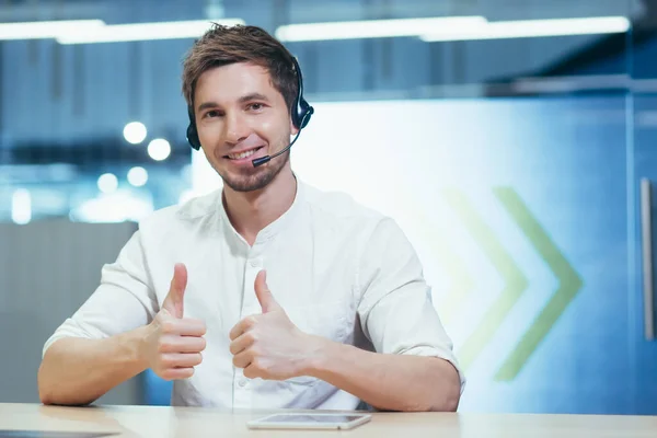 Portrait of male call center employee in modern office, businessman with call headset looking at webcam and having fun talking to client