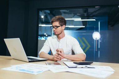 Modern ofiste çalışan genç finans işadamı, dizüstü bilgisayarlı adam çizelgeler ve çizelgelerle çalışıyor.