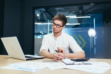 Modern ofiste çalışan genç finans işadamı, dizüstü bilgisayarlı adam çizelgeler ve çizelgelerle çalışıyor.