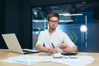 Modern bir ofiste belge ve çizelgelerle çalışan işadamı, erkek denetçi şirketin mali raporunu doğruluyor