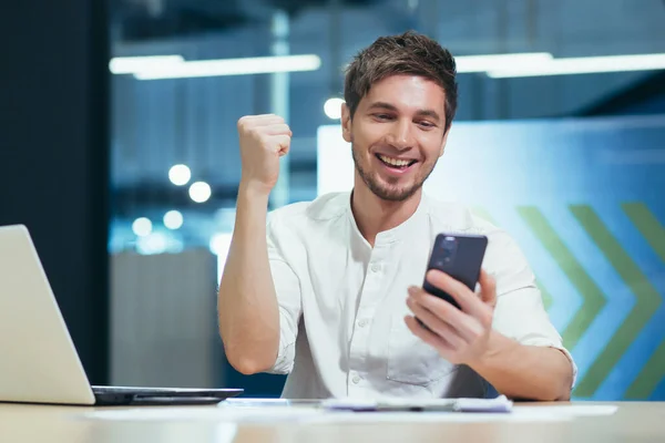 Young businessman received good news smiling and happy reading a message on the phone, man working in a modern office