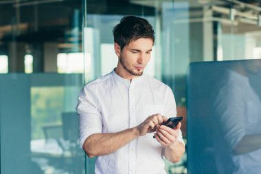 Genç yakışıklı erkek işadamı ofiste cep telefonu kullanıyor. Bir mesaj alır