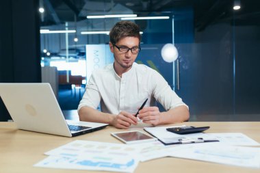 Genç yakışıklı bir adamın portresi, muhasebeci, yönetmen, iş adamı, menajer. Ofiste gözlüklerle oturuyor, bilgisayarla, hesap makinesiyle ve belgelerle çalışıyor..