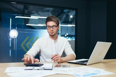 Genç yakışıklı bir adamın portresi, muhasebeci, yönetmen, iş adamı, menajer. Ofiste gözlüklerle oturuyor, bilgisayarla, hesap makinesiyle ve belgelerle çalışıyor..