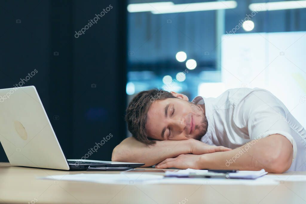 Young handsome man freelancer, businessman, manager in the office at the table resting, fell asleep in his arms at the table, tired