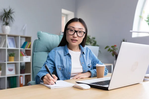 Portrait of young asian woman in office doing paperwork, smiling and looking at camera business woman with laptop in asia.