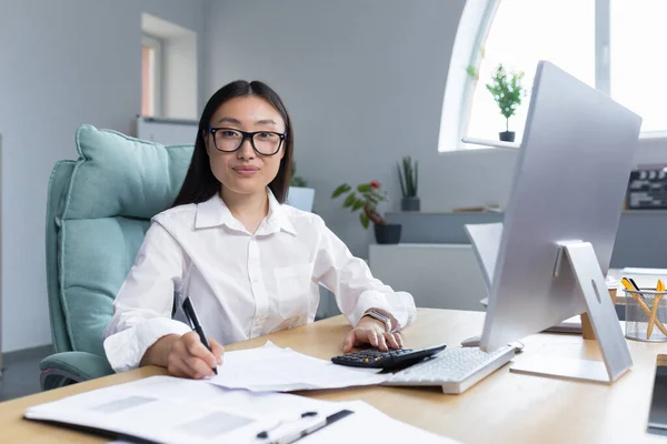 Portrait of young beautiful and successful Asian business woman, female employee smiling and looking at camera, accountant financier paperwork.