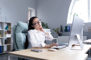 Aşırı yorgun Asyalı kadın ofis çalışanı, boyun ağrısı, elle boyun kası masajı, bilgisayardaki kadın çalışan..