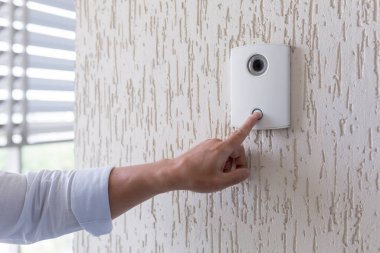 Hand of a man in a white shirt pressing the button of a door knocker on a white wall of a house, a smart door knocker with a video camera for communication