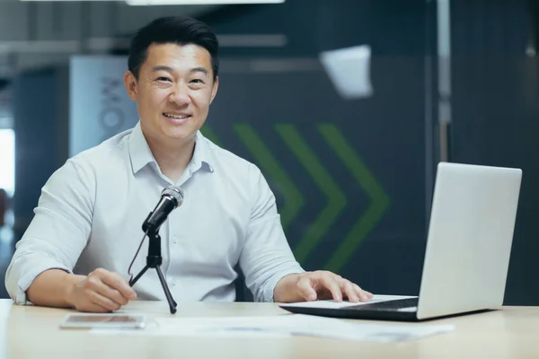 Online radio podcast, male Asian business coach recording online stream, businessman using professional microphone and laptop, portrait of business teacher in office.