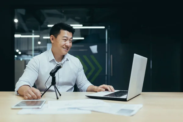 Business coach recording audio podcast, man working in office using professional microphone and laptop to record online stream, radio and podcast, Asian successful businessman