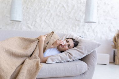Depresyonda, evde yalnız başına oturan, ağlayan, kanepede yatan, üzgün genç bir kadının yakın plan fotoğrafı.