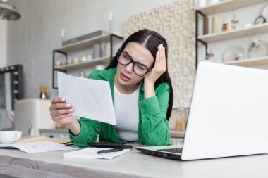 Distressed young woman sit on couch at home read bad negative news in paper correspondence, unhappy biracial female stressed consider unpleasant message in postal letter
