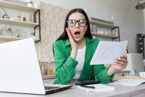 Portrait woman at home, received bad news a letter from the bank, brunette doing paperwork at home in the kitchen, counting bills and summarizing financial documents, shocked bad result looks camera