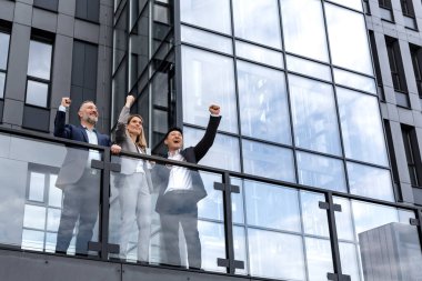 Diverse business group of people colleagues in business clothes outside office building, male and female employees rejoice and celebrate victory hold hand up and smile successful team