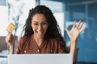 Close-up photo portrait of happy shocked woman, buyer holding bank credit card in hands, business woman looking satisfied in laptop, successful purchase in online internet store