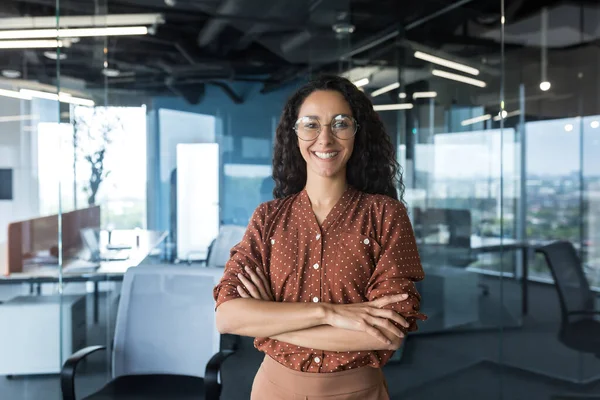 Young successful Indian IT developer female engineer working inside the office of a development company portrait of a female programmer with curly hair and glasses, smiling and looking at the camera.