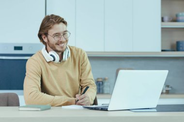 Genç bir girişimci evde kağıt işleriyle uğraşıyor, masada mutfakta oturuyor, uzaktan kumandalı bir bilgisayar kullanıyor..