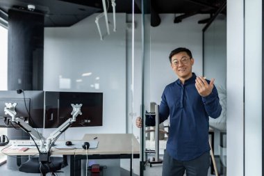 Başarılı bir mühendis patronu ofisine davet eder, gömlek ve gözlüklü Asyalı bir adam kameraya bakar ve gülümser ve karşıdakine el sallar..