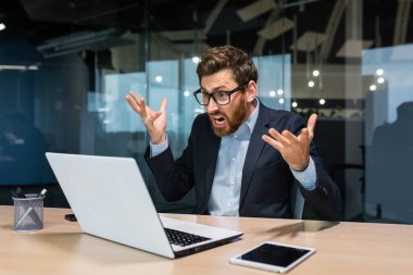 Sinirli ve kızgın iş adamı video görüşmesinde konuşuyor, iş arkadaşlarıyla konuşuyor ve tartışıyor, modern ofis binasında çalışan olgun patron, dizüstü bilgisayarı ve sakalı olan kıdemli adam..