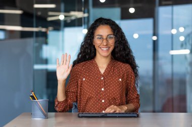 Web kamerası görüntüsü, mutlu ve gülümseyen Latin Amerikalı kadın gülümseyen ve kameraya bakan selamlama hareketi, teknik destek ve müşteri hizmetleri çalışanı, online yardımdan.