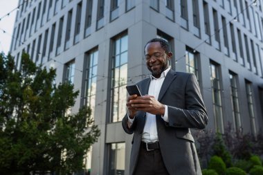 Olgun Afro-Amerikan patronu telefon kullanıyor, ofis binası dışında takım elbiseli ve gözlüklü iş adamı mesaj yazıyor ve internette gülümseyen sayfaları karıştırıyor..