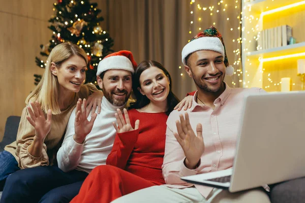 diverse friends celebrating New Year and Christmas together home, Christmas party with guests, men and women smiling and happy together talking on video call greeting friends remotely, using laptop.