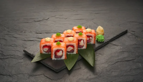 Rollos de sushi con atún salmón unagi y aguacate en un plato de piedra negra. —  Fotos de Stock