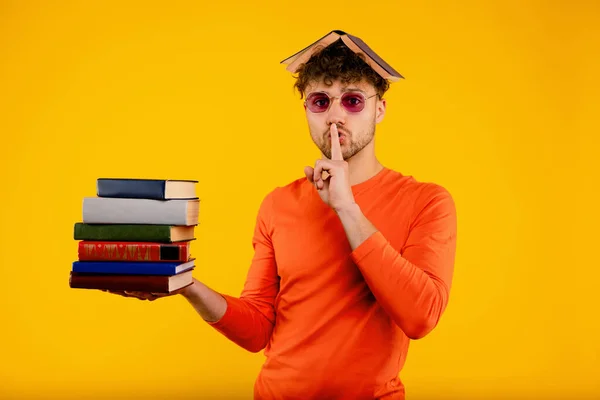 彼の頭の上に本を持つ若いハンサムな男 本を保持することは 試験のための沈黙のサインを示しています 黄色の背景 高品質の写真 — ストック写真