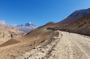 Muktinath Sadak. Muktinath yolu boyunca yürüyüş direkleri olan bir grup turist. Arka planda Yakwakang Dağı.