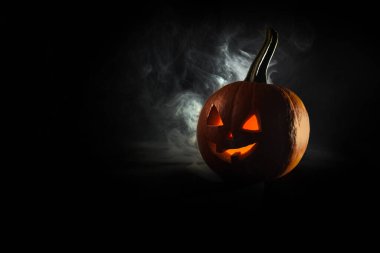 Cadılar Bayramı, siyah arka planda parlak yüzlü turuncu balkabağı. Kalın duman çıkıyor..