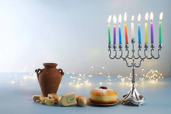 Jewish holiday Hanukkah background with menorah- traditional candelabra, spinning top and doughnut on blue background