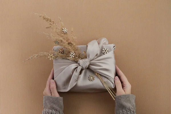 Zero rifiuti Natale piatto laici. Mani che tengono il regalo di Natale semplice in stile furoshiki. Stile di vita sostenibile libero di plastica — Foto Stock